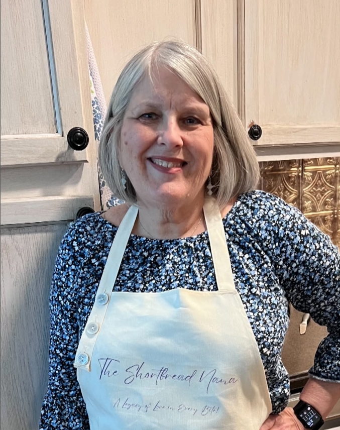 Lovely smiling woman in her kitchen wearing an apron that says The Shortbread Nana.