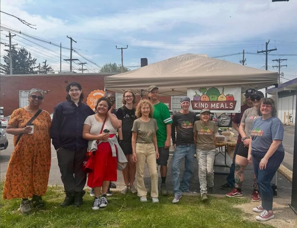 A group of people standing in front of a tent with a sign that says Kind Meals.